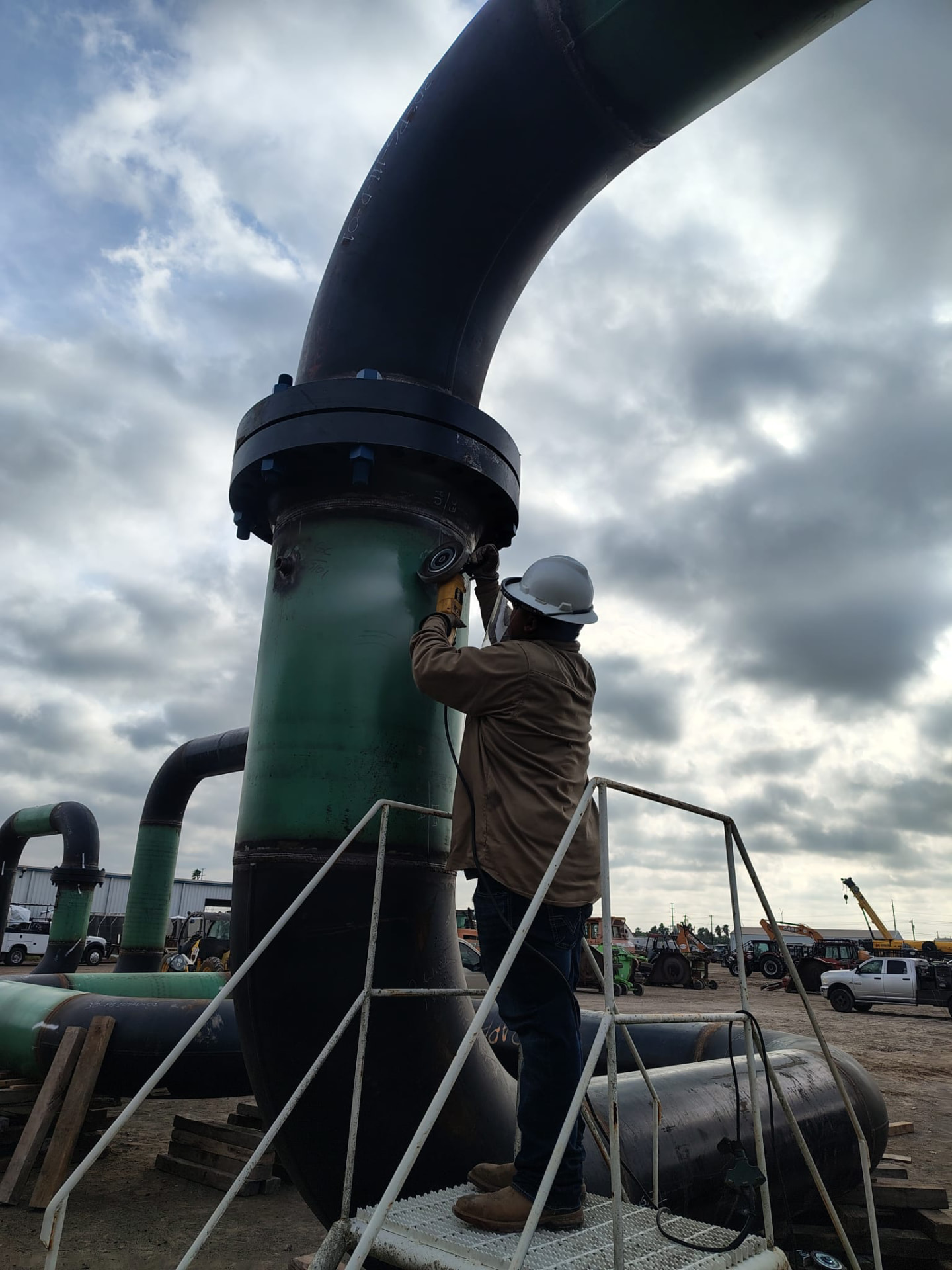 Welder grinding a large-diameter flanged pipe spool on a work platform
